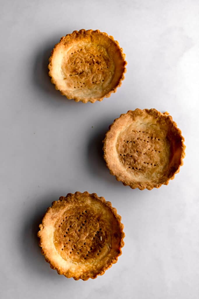 Three baked tart shells on white marble.