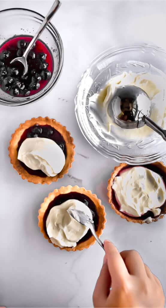 Cream cheese scooped on top of blueberry preserves in  mini tart shells