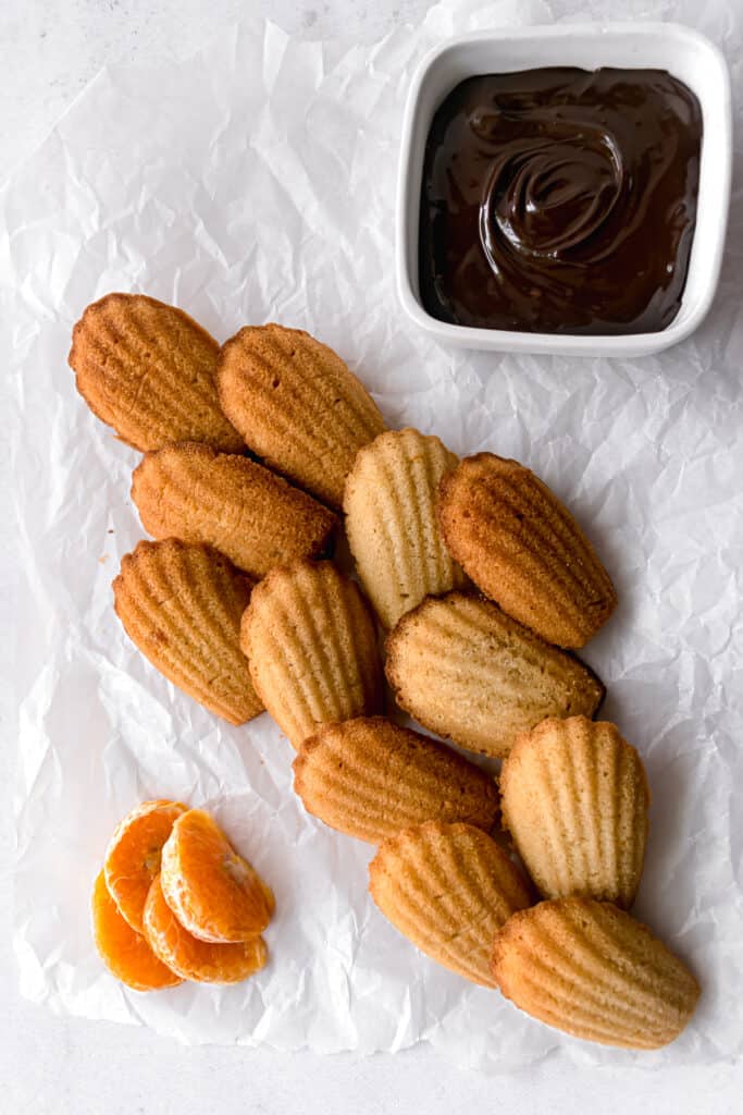 Orange madeleines ready to be glazed with chocolate on a white marble