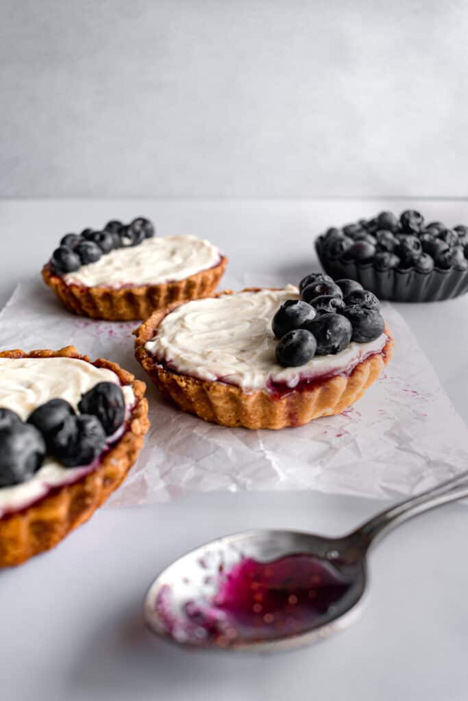 Mini blueberry tarts with cheesecake filling on a white parchment paper