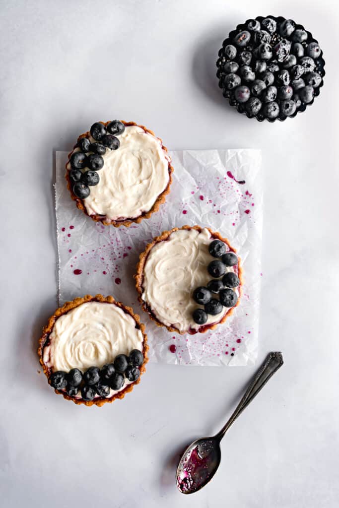 Three mini tarts and fresh blueberries on a white marble