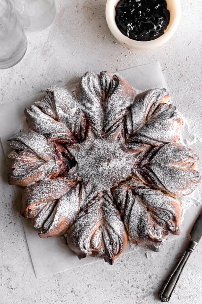 Baked Blueberry jam cream cheese star bread on a parchment paper dusted with powdered sugar