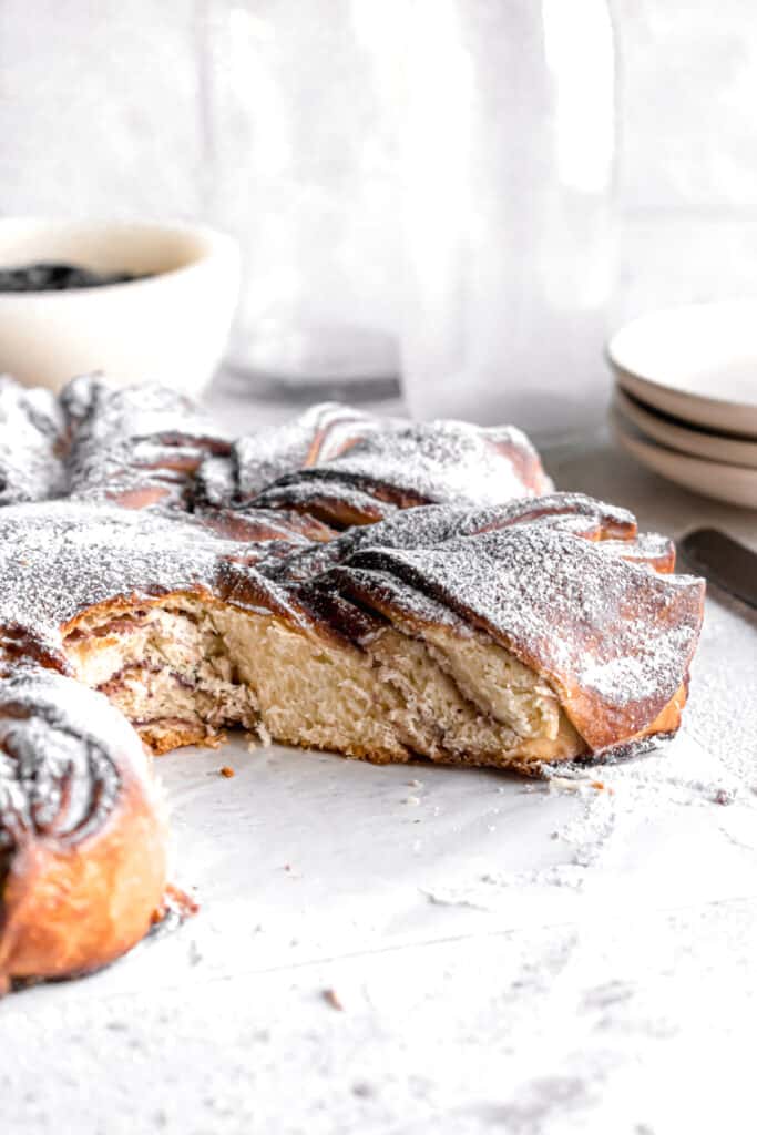 Baked Blueberry jam cream cheese star bread on a parchment paper dusted with powdered sugar with one slice cut