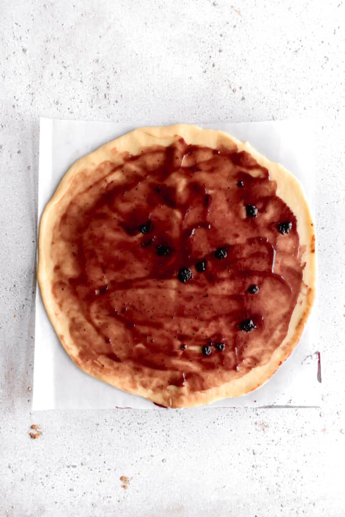 yeast dough for star bread on a parchment paper rolled out into a circle and layered with blueberry jam