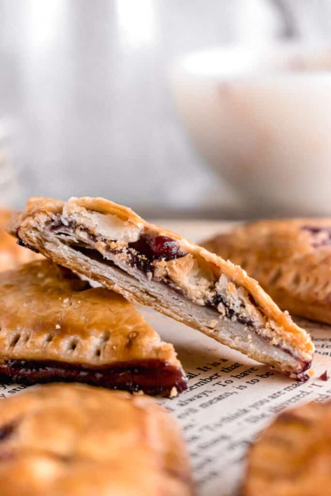 Heart shaped mini blueberry pies on a wooden board with one cut into two parts with flaky layers of pie crust