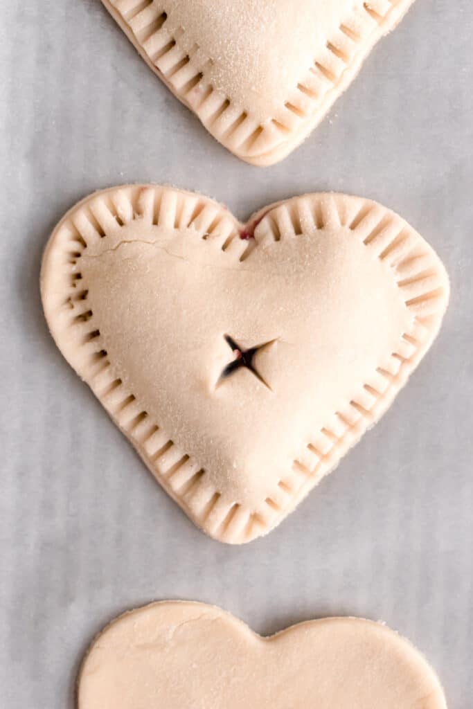 Pie dough cut into hearts with a heart shaped cookie cutter topped with blueberry jam and sealed with another heart