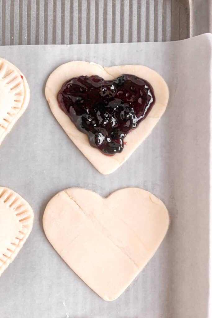 Pie dough cut into hearts with a heart shaped cookie cutter topped with blueberry jam