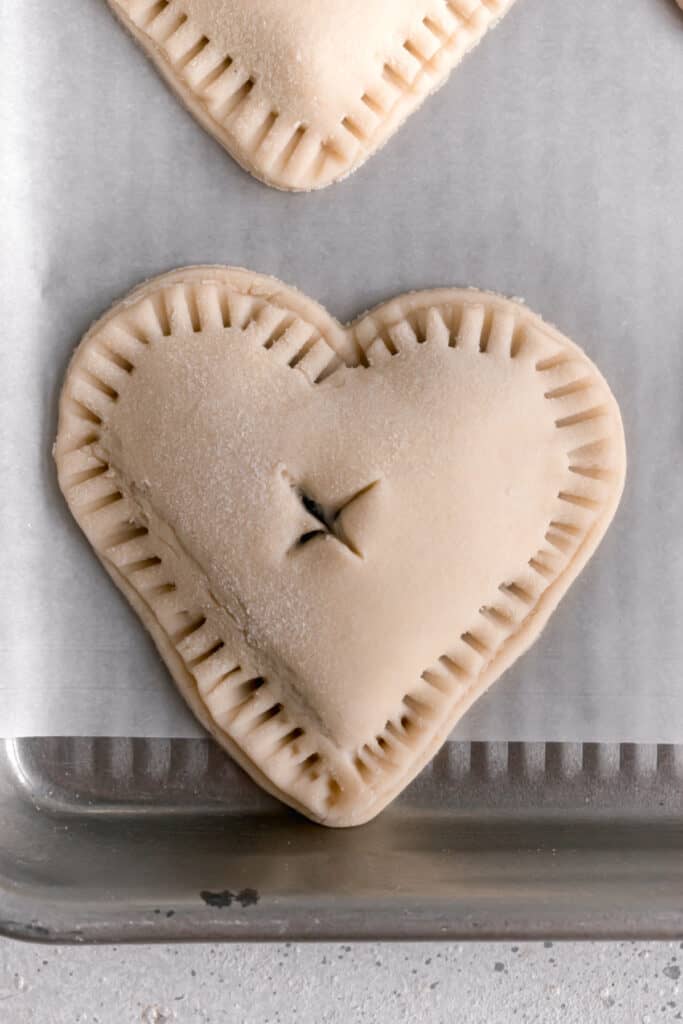 Pie dough cut into hearts with a heart shaped cookie cutter topped with blueberry jam and sealed with another heart