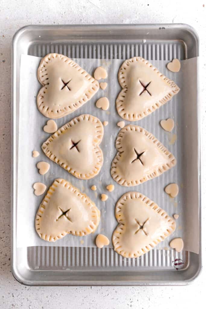 Pie dough cut into hearts with a heart shaped cookie cutter topped with blueberry jam and sealed with another heart brushed with egg wash